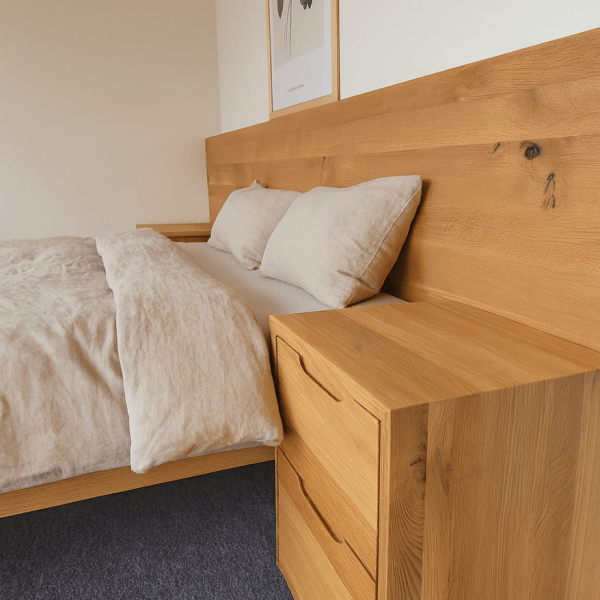 Wooden bed frame with beige bedding and a matching nightstand in a simple bedroom setting.